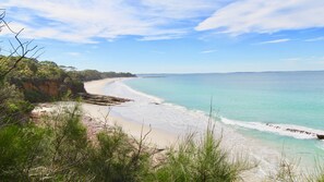 A coastal landscape with a sandy beach, clear turquoise waters, and a rocky cliff with vegetation. - On Collingwood Beach  by Book Jervis Bay - Downstairs Apartment - 50m From THE Water (Vincentia)