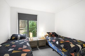 A bedroom with two beds, a window, and a nightstand with a lamp. - Apartment 36 Pacific Apartments (Lorne)