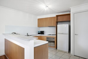 A modern kitchen with white cabinetry, a built-in microwave, a stove, and a refrigerator. - Apartment 36 Pacific Apartments (Lorne)