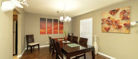 A dining room with a wooden table, six chairs, a vase with flowers, and two wall art pieces.