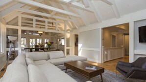 Un salón amplio con un sofá seccional grande, una mesa de centro y un sillón oscuro. La habitación cuenta con vigas de madera a la vista y un techo alto.
