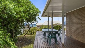 Un espace extérieur aménagé en terrasse, avec une table et des chaises, entouré de verdure et offrant une vue sur la mer.