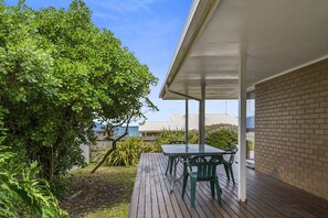 Eine Terrasseneinrichtung im Freien mit Tisch und Stühlen, umgeben von Grünpflanzen und Blick aufs Meer.