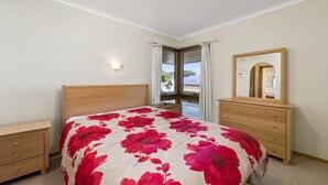 Une chambre à coucher comprenant un lit, une commode, une table de chevet, une fenêtre avec des rideaux et un miroir.