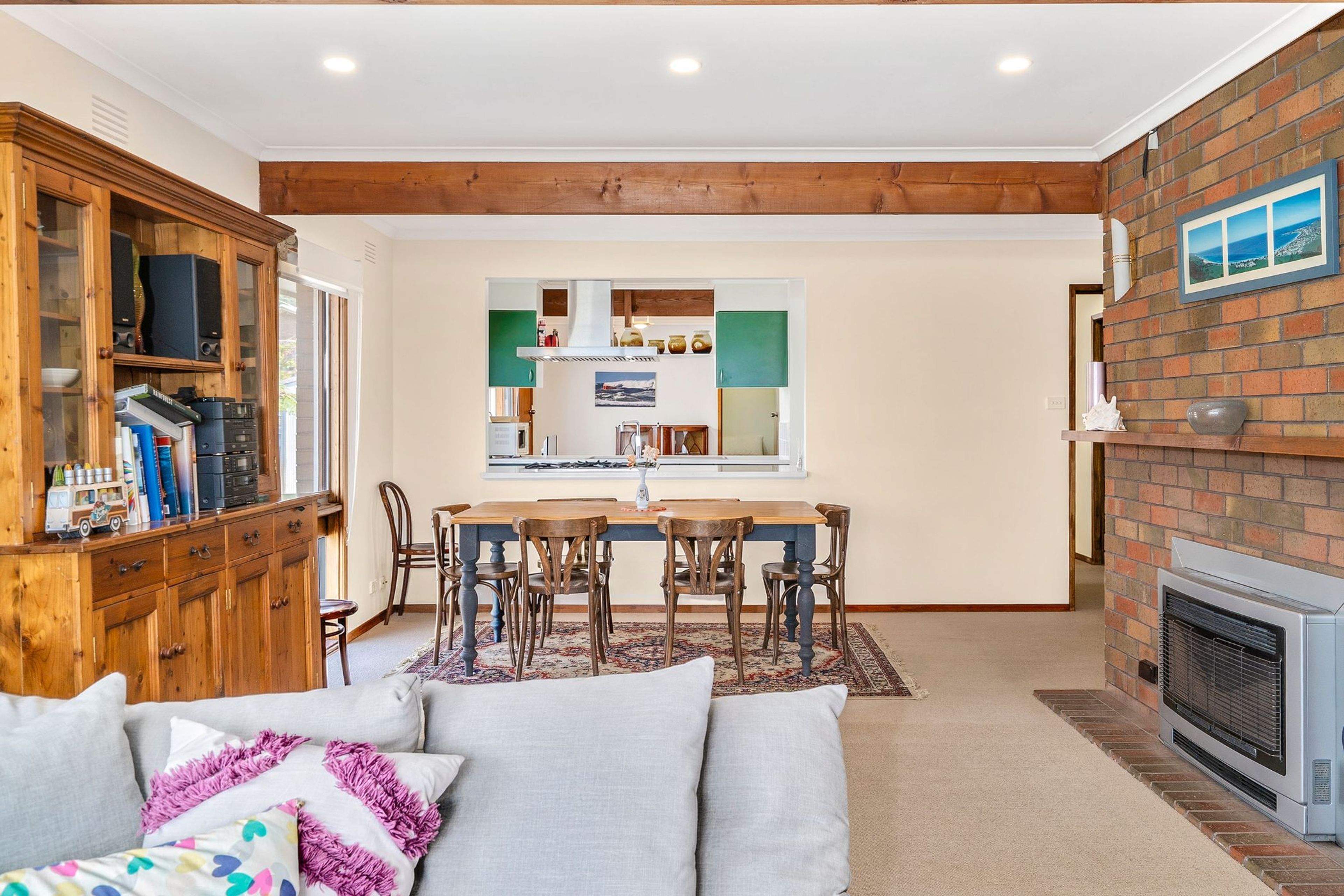A cozy living room with a fireplace, a dining area with a view of the kitchen, and a wooden cabinet with various items.