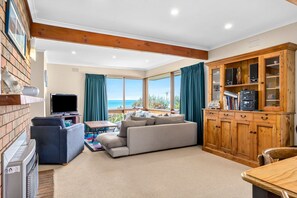 A spacious living room with a large window, a sofa, a television, and a wooden cabinet. - Sea-Esta - Room For All The Family (Apollo Bay)