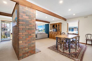 A spacious living area with a brick fireplace, a dining table with chairs, a sofa, and a view of the outdoors.