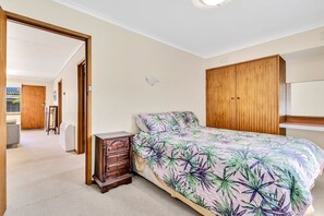 A bedroom with a bed, a wooden wardrobe, a nightstand, and a door leading to another room. - Sea-Esta - Room For All The Family (Apollo Bay)