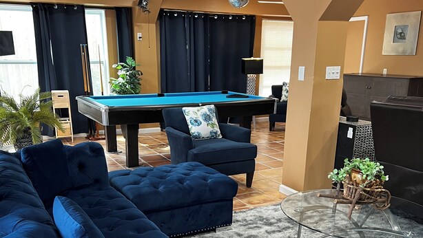 A living room with a pool table, dark blue sofas, a glass coffee table, and a ceiling fan. - Beautiful 2BR 2BA Home with Private Pool & Jacuzzi - Includes Pool Table (Sarasota)