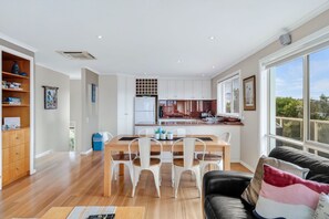 A modern kitchen with white cabinets, a dining table with chairs, and a large window with blinds.