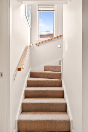 Un escalier avec une rampe en bois, des marches recouvertes de moquette et une fenêtre au-dessus.