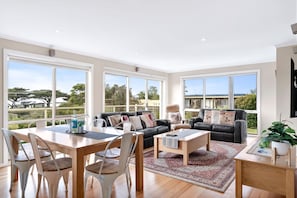 A spacious living room with a dining area, large windows, and a view of the outdoors. - The Dunes 1 (Apollo Bay)