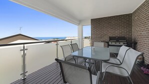A balcony with a glass table and chairs, a brick wall, and a grill.