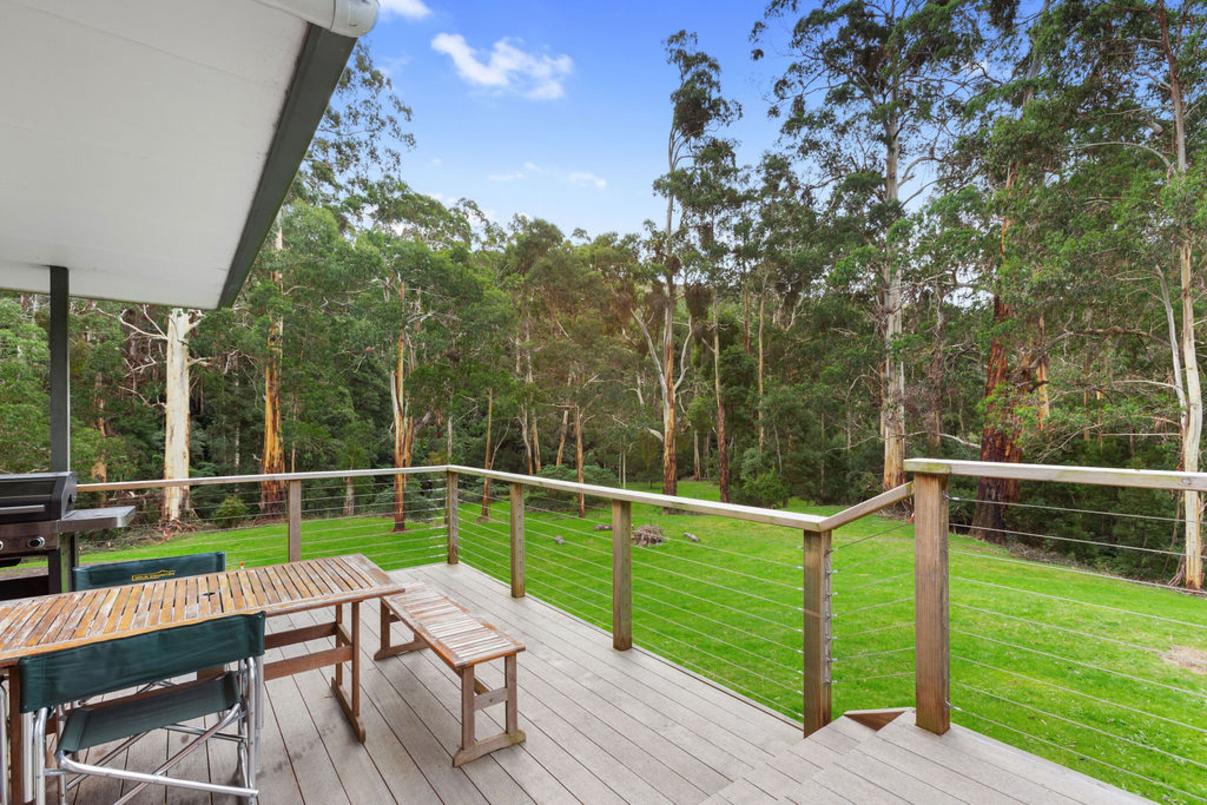 A wooden deck with a table and chairs, overlooking a grassy area with trees.