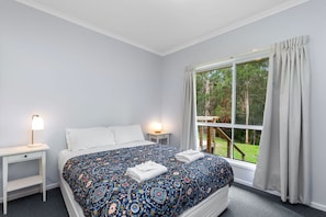 Une chambre à coucher avec un grand lit, deux tables de chevet, une commode et une fenêtre avec des rideaux.