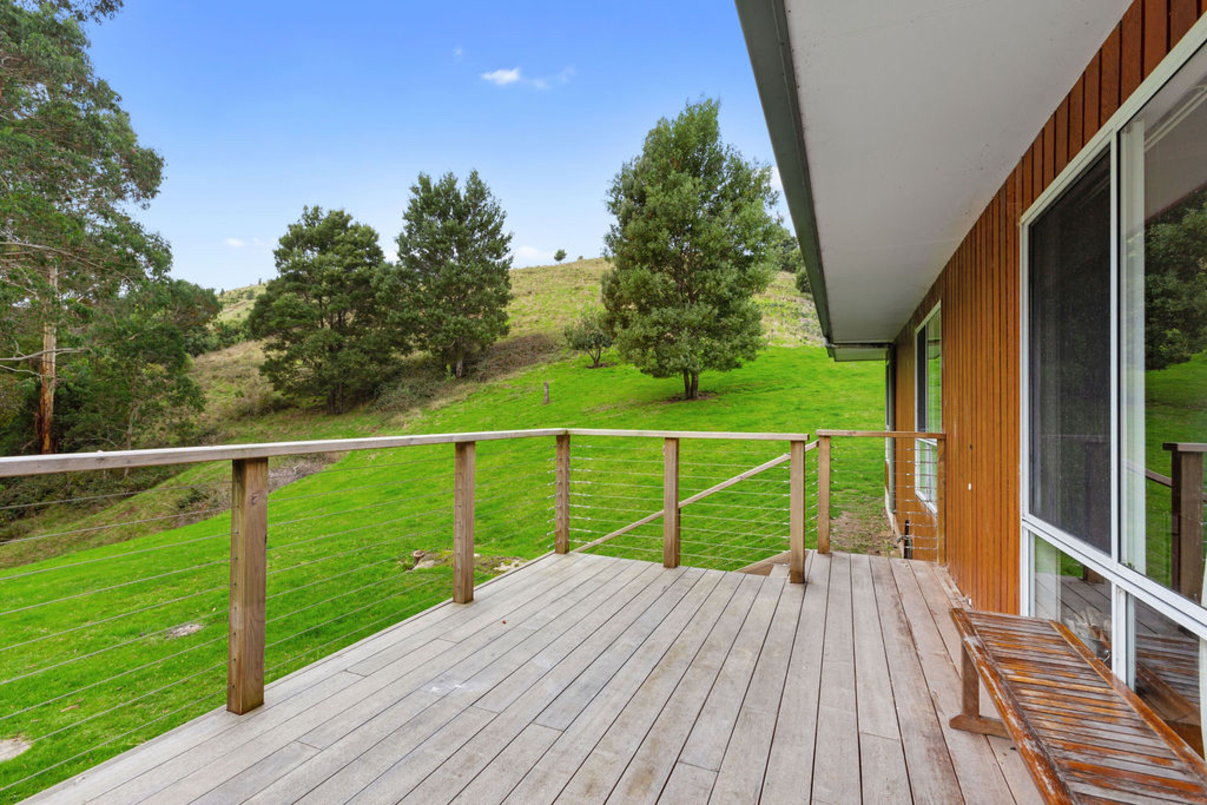 Une terrasse en bois avec une rambarde en métal, donnant sur une colline verdoyante parsemée d’arbres.