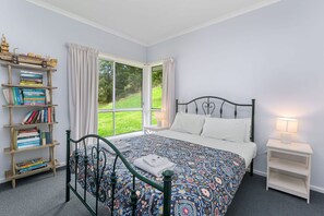 A bedroom with a bed, a window, a bookshelf, and a bedside table.