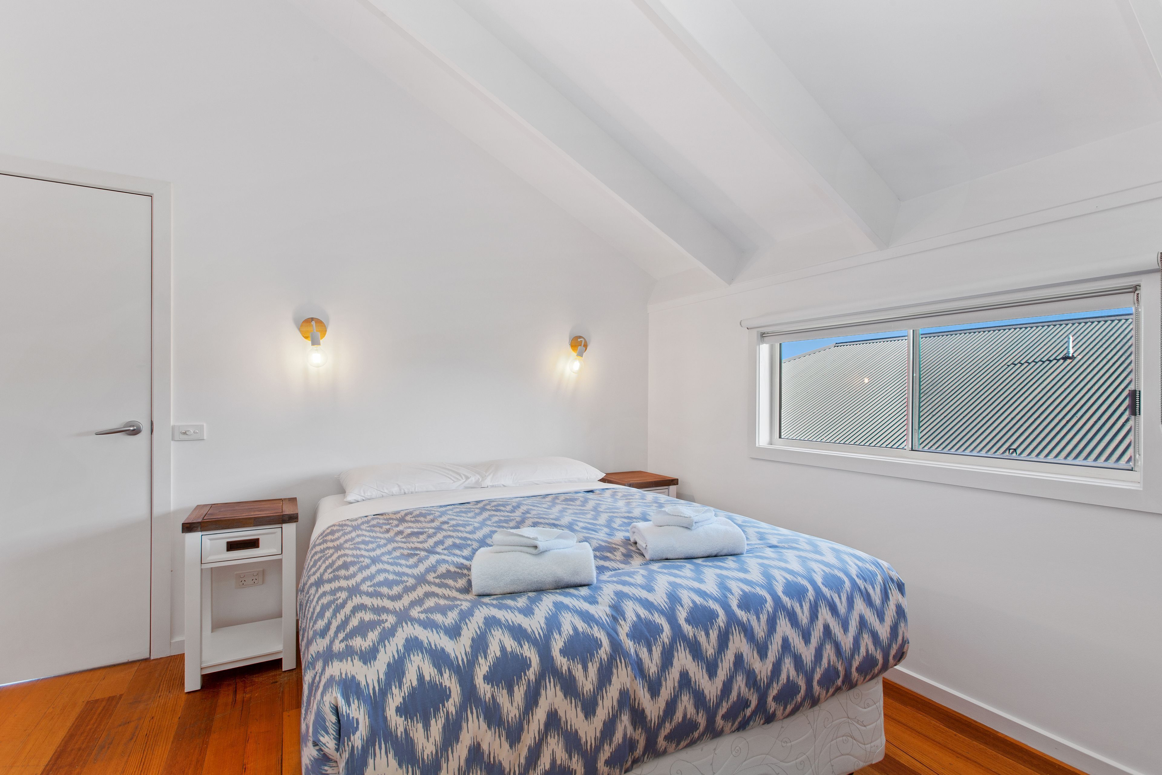 Een slaapkamer met een bed, twee nachtkastjes, een raam met zonwering en een deur.