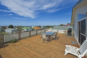 Eine Holzterrasse mit Tisch und Stühlen, ein weißer Zaun und im Hintergrund Häuser und Bäume.