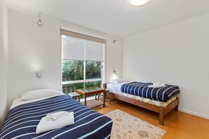 Ein Schlafzimmer mit zwei Betten, einem kleinen Tisch und einem Fenster mit Blick auf Grünflächen.