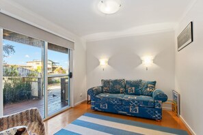 A room with a sofa, two wall-mounted lights, a sliding glass door, and a view of the outside. - Barrabay (Apollo Bay)