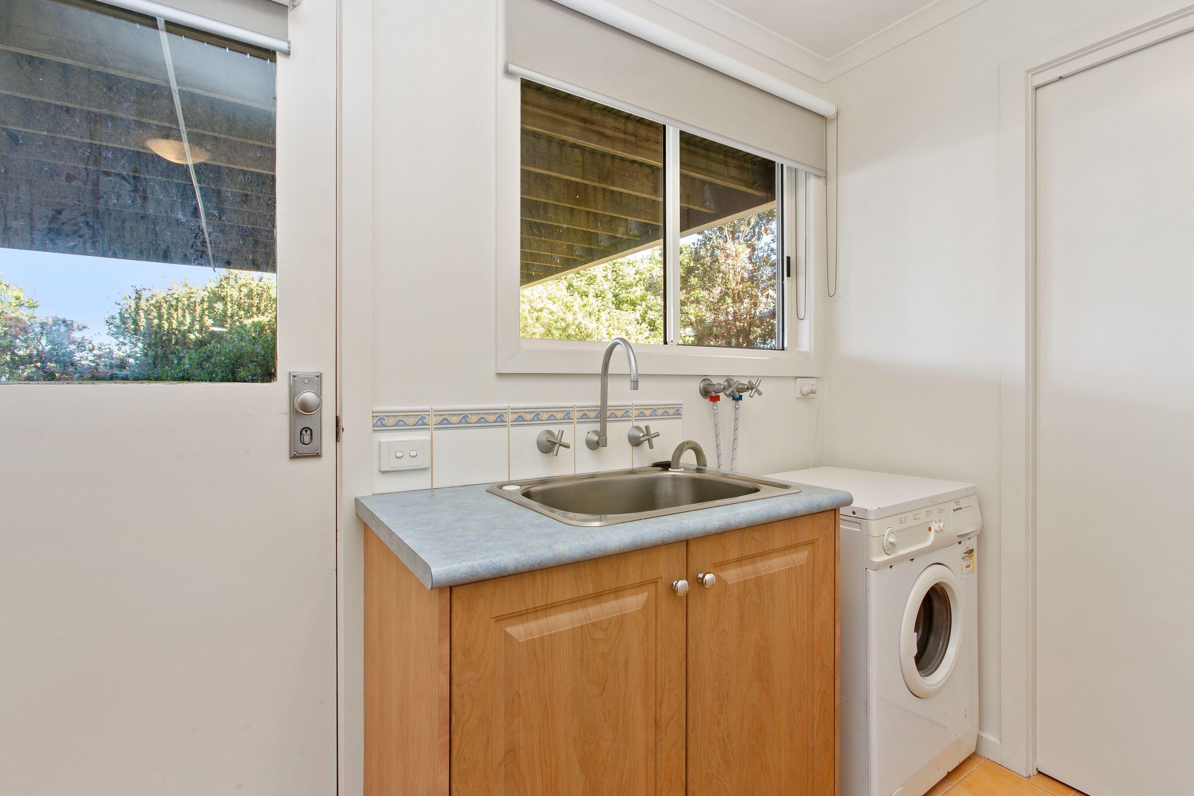 A compact kitchen with a built-in washing machine, a window with a view of greenery, and a sink with a faucet.