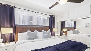 Habitación de hotel con una cama grande, dos mesitas de noche con lámparas, un ventilador de techo y un espejo amplio.