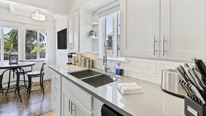 Una cocina moderna con armarios blancos, una isla grande con lavamanos y un comedor con taburetes de bar.