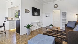 Una sala de estar moderna con comedor, cocina y un televisor grande montado en la pared.