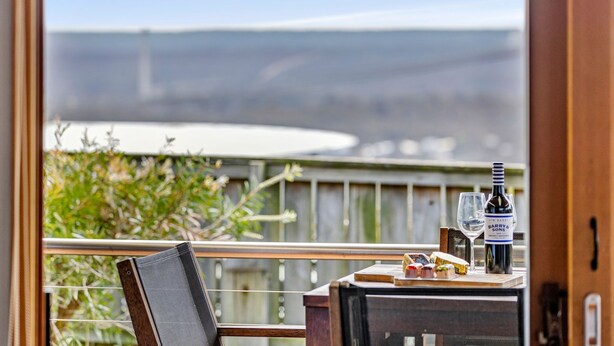 A balcony with a table set for two, a bottle of wine, and a glass. - Blue Water (Anglesea)