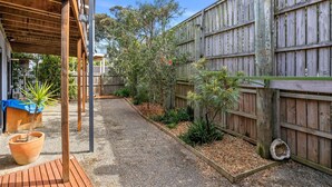 A covered outdoor area with a gravel path, wooden deck, and a variety of plants. - Blue Water (Anglesea)