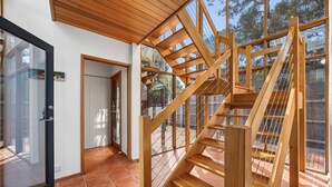 A modern interior with a wooden staircase, glass doors, and a tiled floor. - Blue Water (Anglesea)