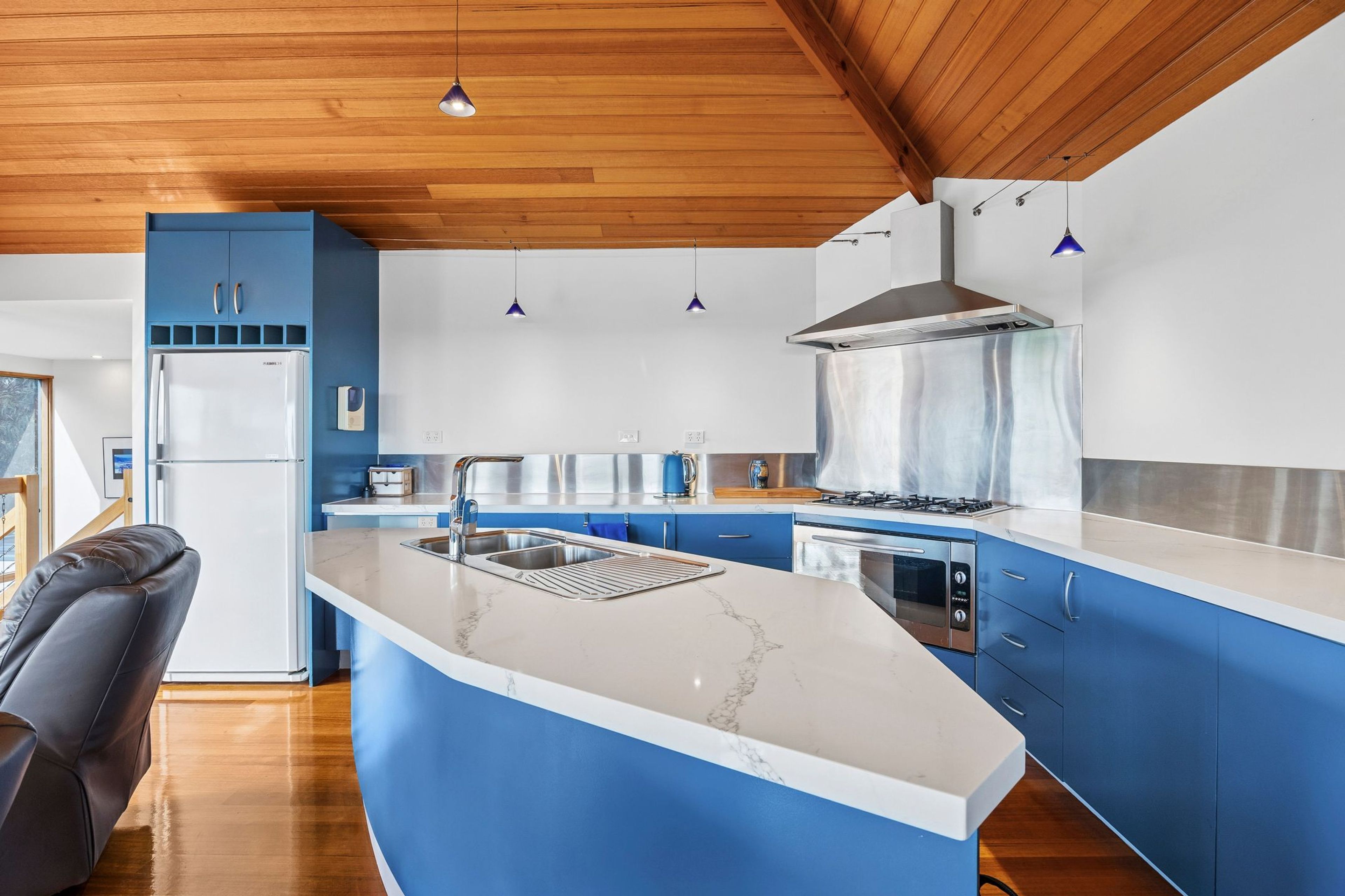 Una cocina moderna con armarios azules, una campana extractora de acero inoxidable y una encimera de mármol.
