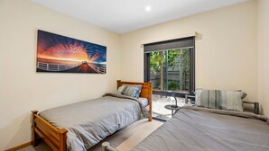 A bedroom with two single beds, a large window, and a painting of a sunset. - Blue Water (Anglesea)