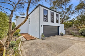 A modern two-story building with a garage, surrounded by trees and gravel. - Blue Water (Anglesea)