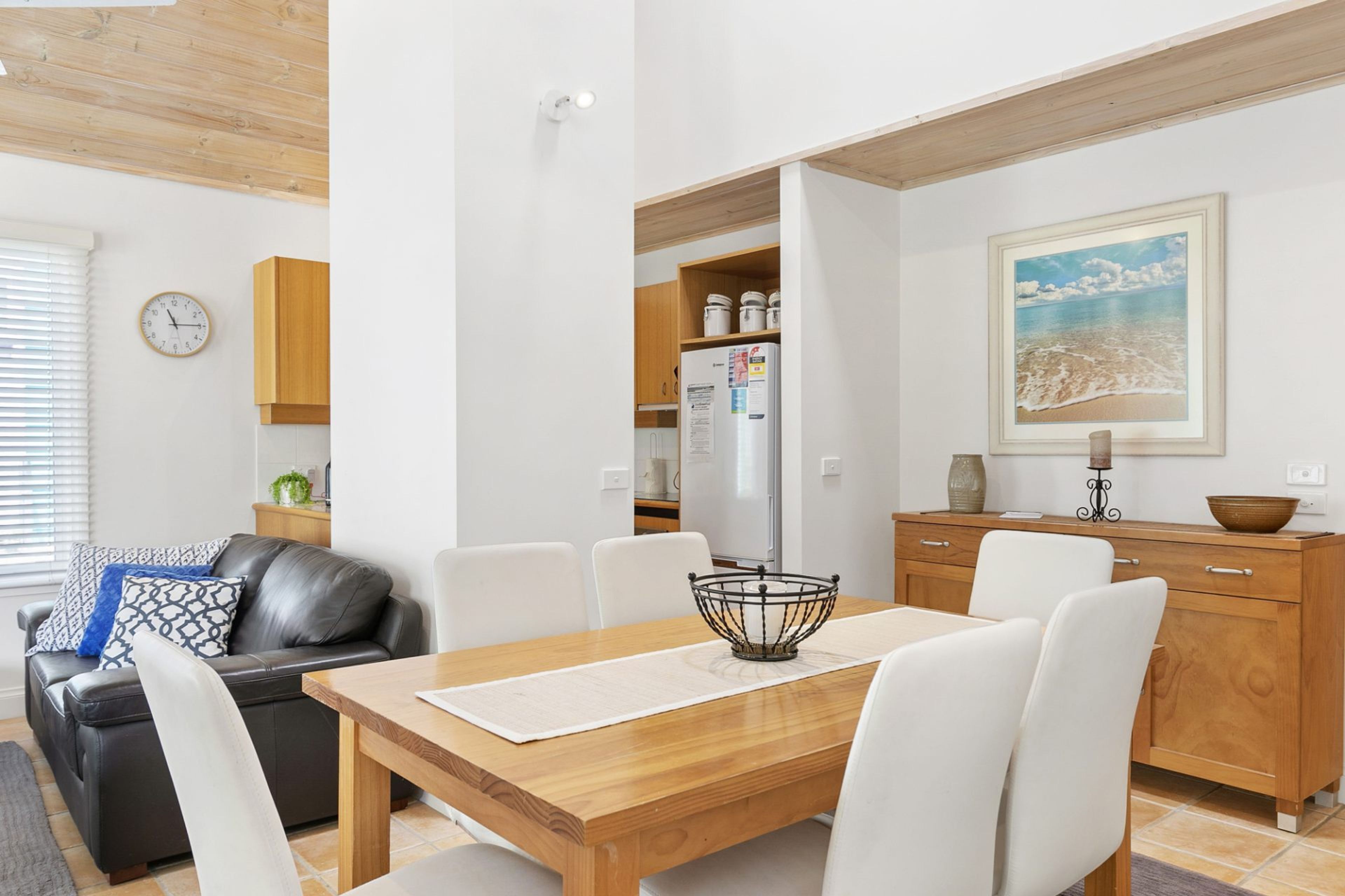 A modern kitchen with white cabinets, a wooden dining table, and a white refrigerator.