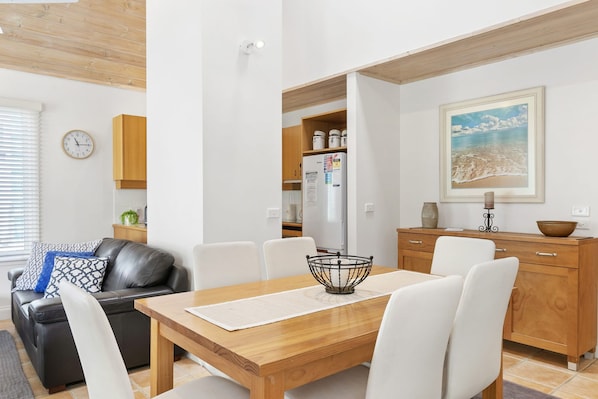 A modern kitchen with white cabinets, a wooden dining table, and a white refrigerator.