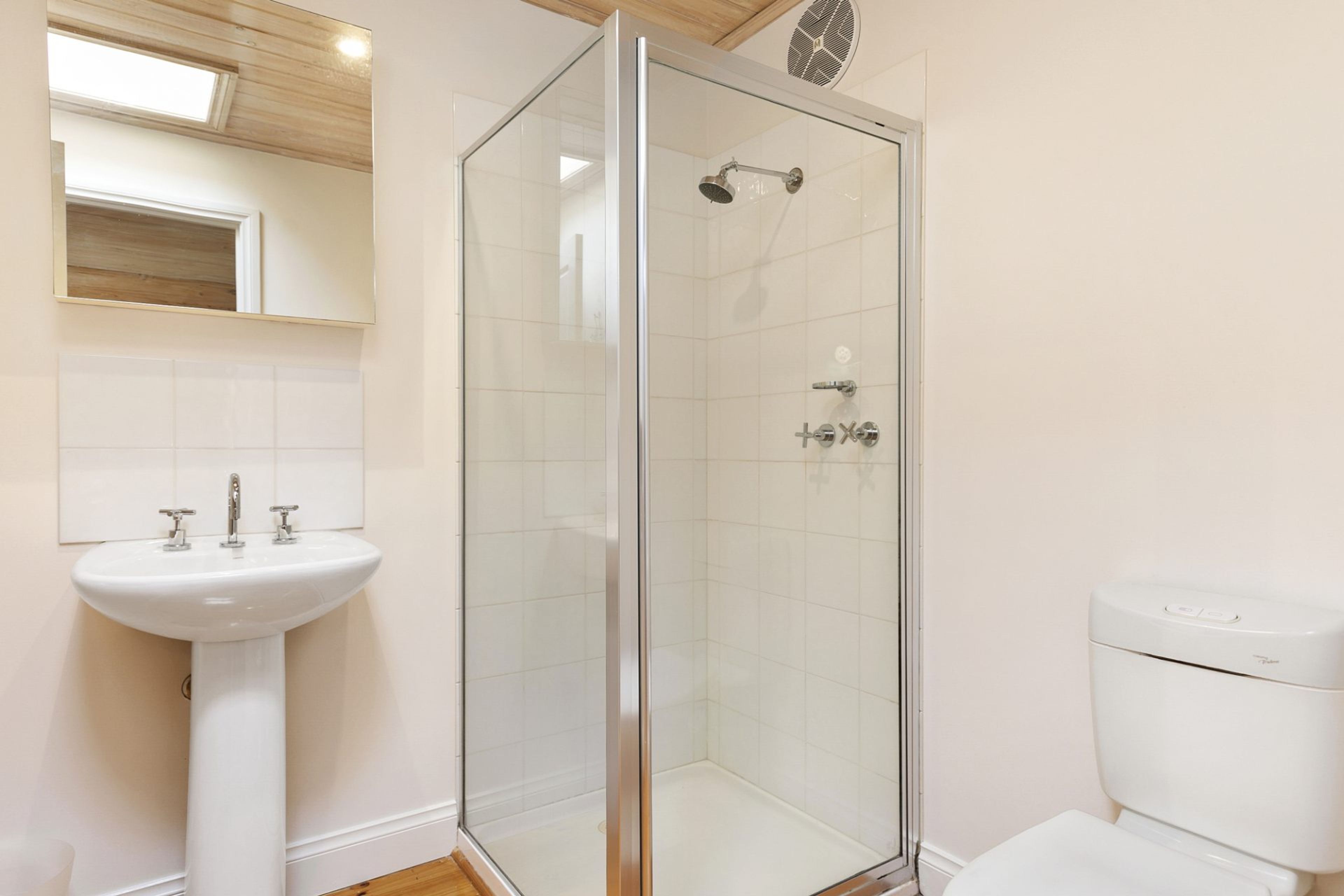 Un baño moderno con ducha envuelta en vidrio, lavamanos pedestal y retrete.