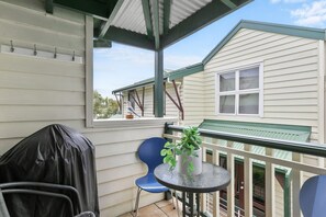 A covered balcony with a table, chairs, and a potted plant.