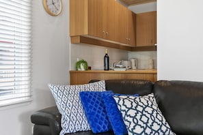 A living room with a brown leather sofa, patterned cushions, and a window with blinds.