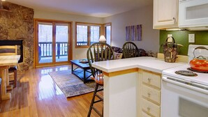 A cozy kitchen with a stone wall, wooden dining table, and chairs. There is a white countertop with a kettle and a microwave. - Great Value! Epic Slope Views-Hot Tub+ Steps to Eat/Drink/Shops/Free Bus-W/D in Unit-Gas Fireplace (Steamboat Springs)