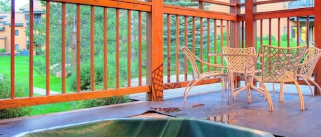 Uma banheira de hidromassagem em um deck de madeira, com vista para um gramado verde e edifícios ao fundo.