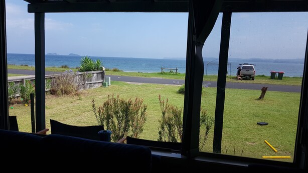 A view from a window overlooking a grassy yard with a road, a parked vehicle, and a body of water in the distance.