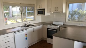 A compact kitchen with white cabinets, a built-in microwave, a stove, and a dishwasher.
