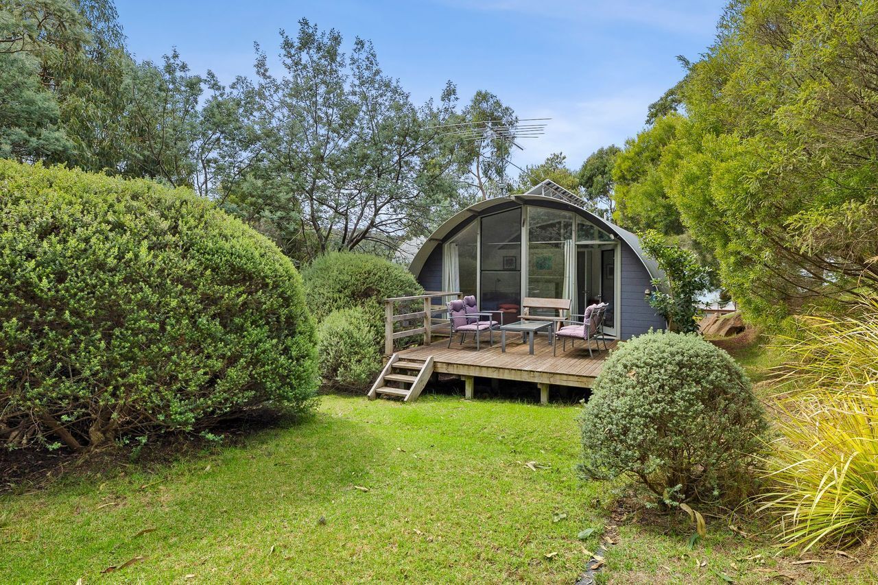 A glass-enclosed structure with a deck, surrounded by well-maintained greenery.