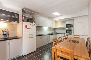 Eine moderne Küche mit weißen Schränken, einem eingebauten Backofen, einer Kaffeemaschine und einem Esstisch mit Stühlen.