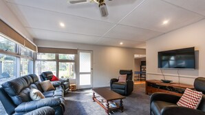 A modern living room with a leather sofa, a coffee table, a recliner, and a flat-screen TV mounted on the wall. - Oceans 12 (Anglesea)
