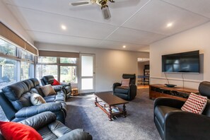 Ein modernes Wohnzimmer mit einer Ledersofa, einem Couchtisch, einem Liegestuhl und einem flachbildfernseher an der Wand.