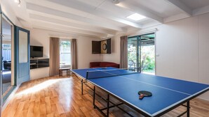 A spacious room with a ping pong table, a television, and a view of greenery through a sliding door. - Oceans 12 (Anglesea)