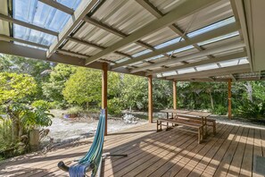 Ein überdachter Außenbereich mit Holzterrasse, einer Hängematte und einem Tisch mit Bank.